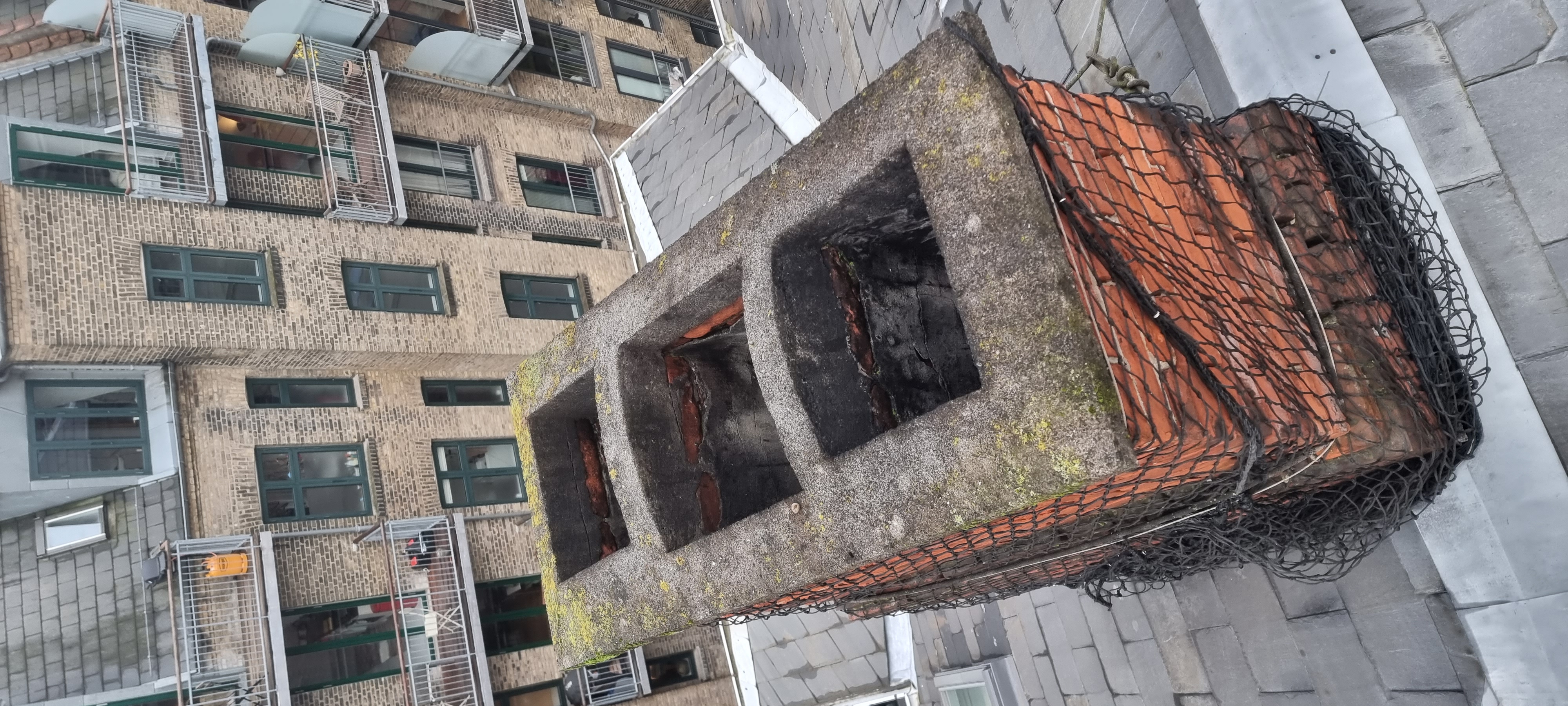 Drone nærbillede af sikkerhedsnet monteret på kritisk skorsten — mursten aktivt bag net